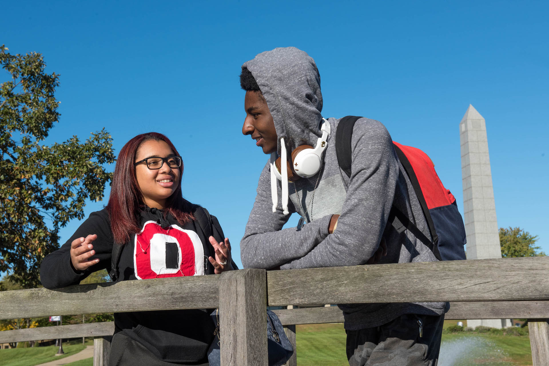 Two students are outside leaning on a rail and talking.