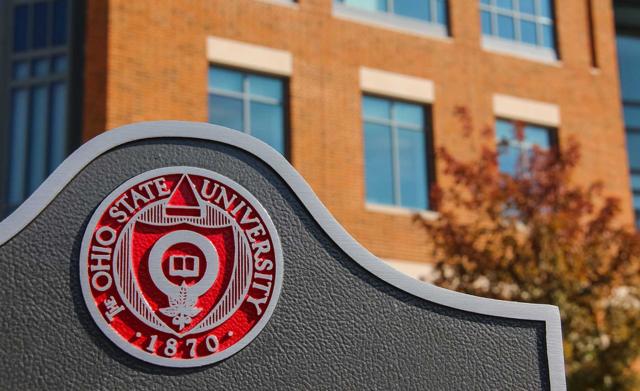 Picture of the seal of The Ohio State University on a sign with a brick building in the background.
